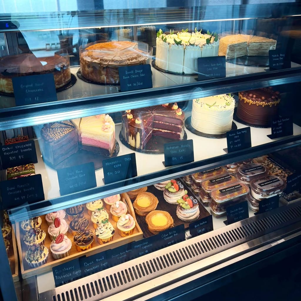 Display case showing burnt cheesecake, devil food chocolate cake, red velvet, pandan gula apong and Dubai kunafa