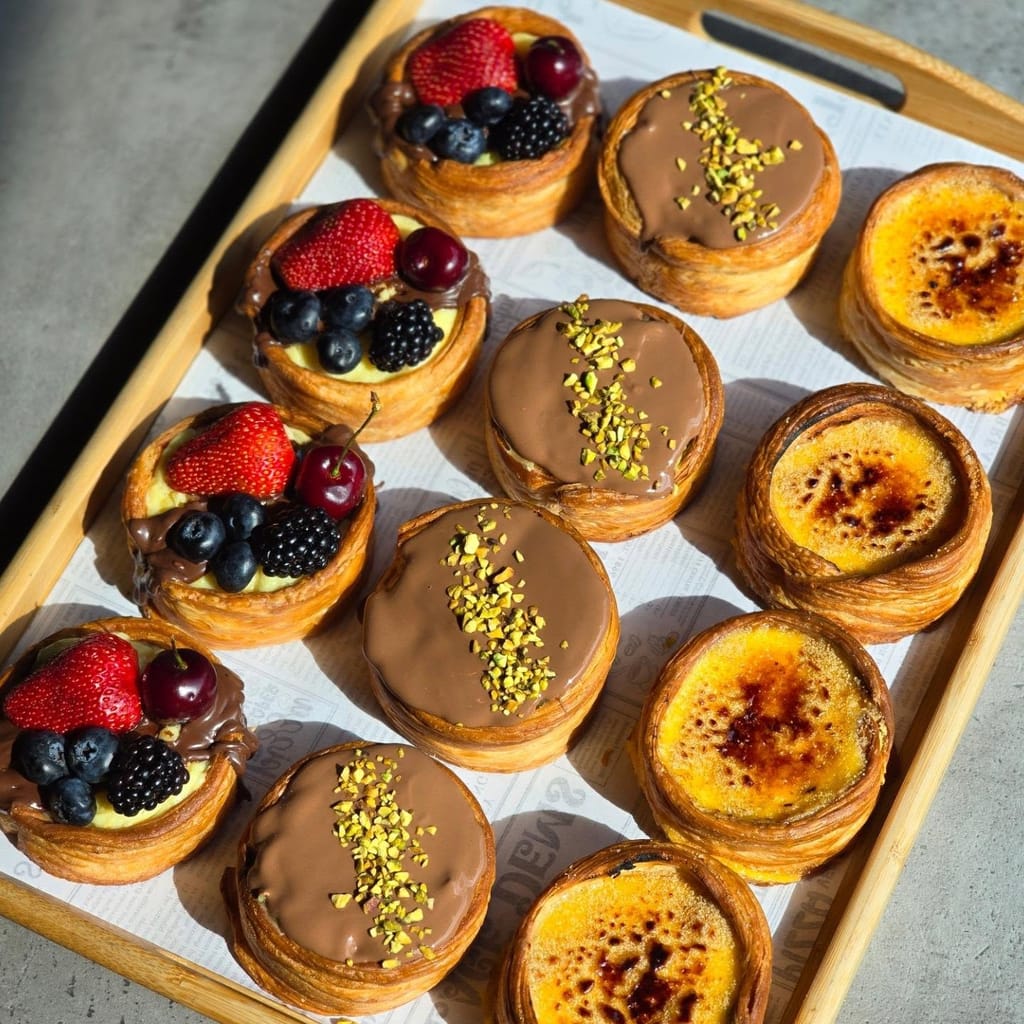 A tray of fresh berry tarts, pistachio danish and torched creme brulee tarts