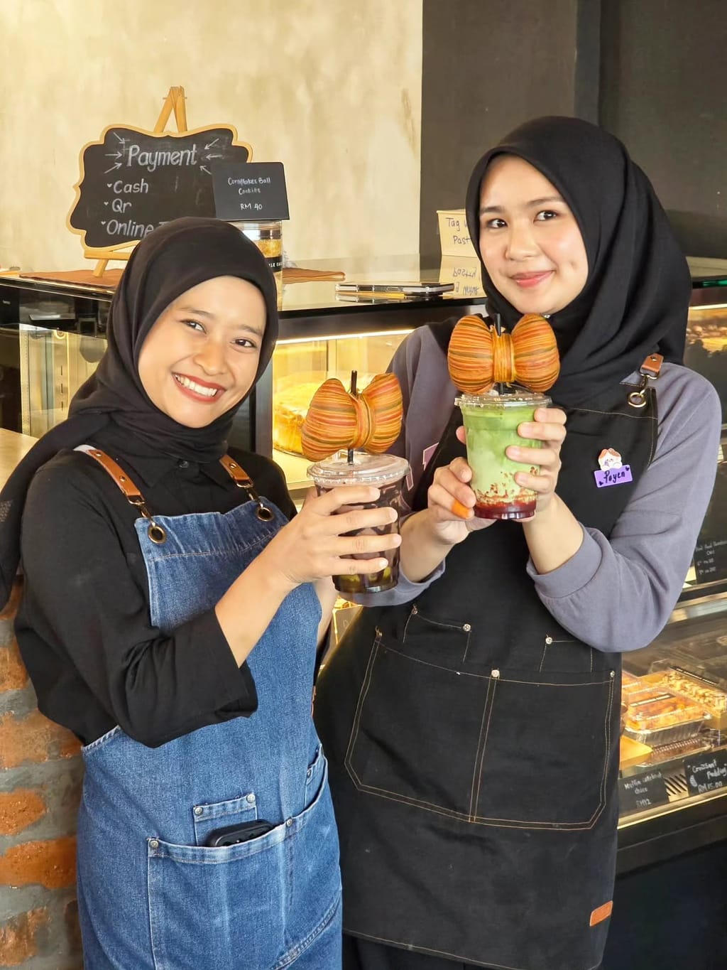 Two team members holding iced drinks by the counter